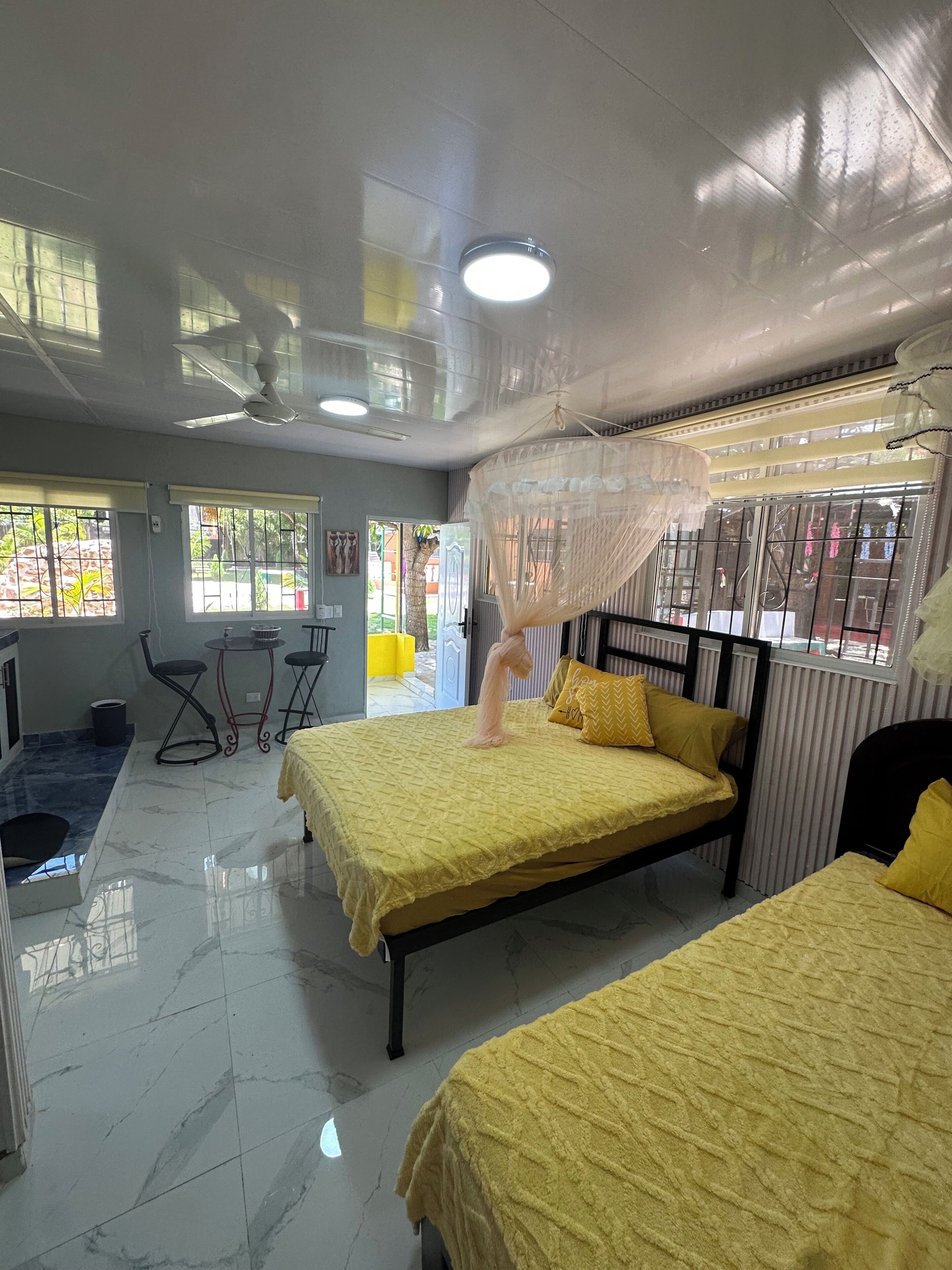 Une chambre d’hôtel avec deux lits, un ventilateur de plafond, une moustiquaire, une petite table et des chaises.