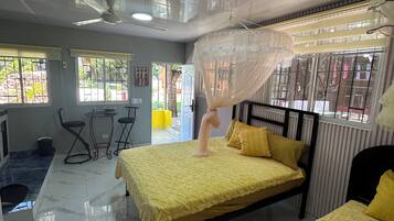 Une chambre d’hôtel avec deux lits, un ventilateur de plafond, une moustiquaire, une petite table et des chaises.