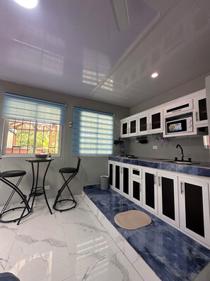 Una cocina con armarios blancos, encimera de mármol y un pequeño comedor con dos sillas.