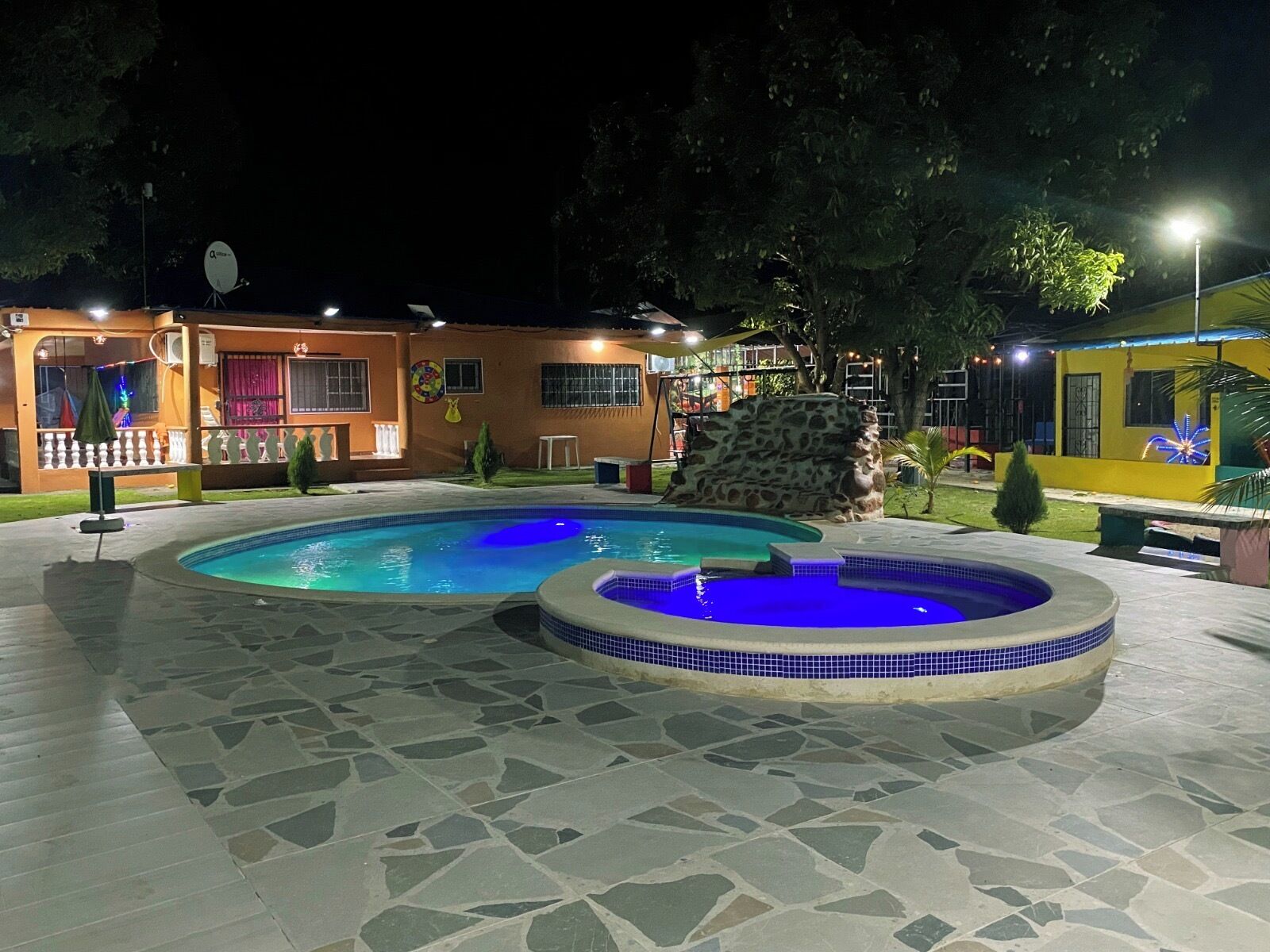 A swimming pool area with two pools, a hot tub, and a stone wall.