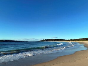 A beach with clear skies, gentle waves, and a distant forested landmass. - Murramarang Haven at Bawley Point (Bawley Point)
