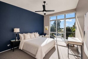 A bedroom with a bed, bedside tables, a lamp, a ceiling fan, and a large window with a view of trees and a building. - Murramarang Haven at Bawley Point (Bawley Point)