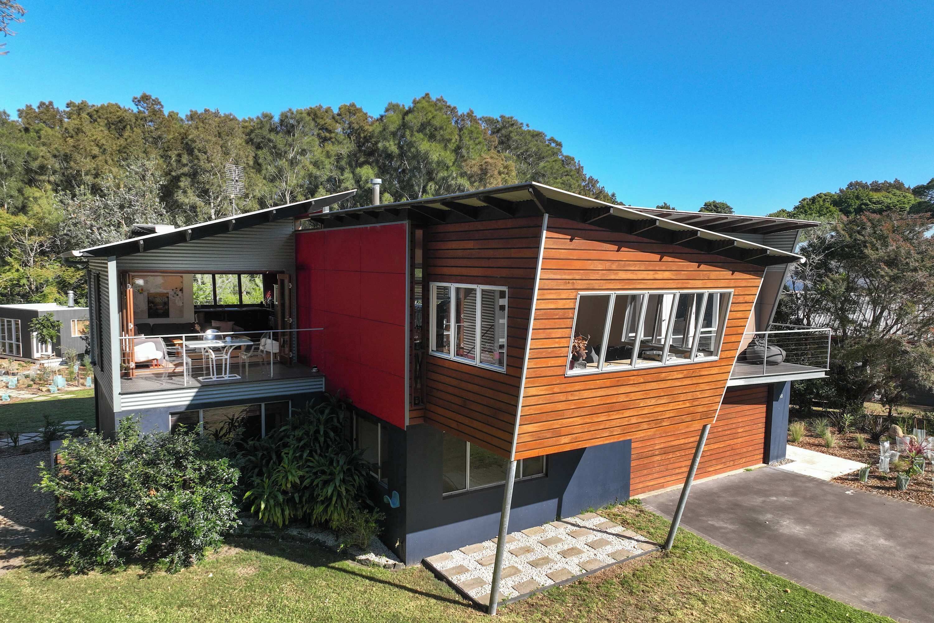 Uma casa moderna com varanda, parede externa vermelha e vista para a floresta ao redor.