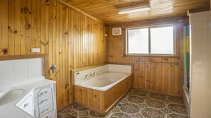 Ein Badezimmer mit Holzverkleidung, einer Badewanne, einem Waschbecken und fliesenbesetztem Boden.