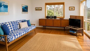 Una sala de estar con sofá, televisor, mueble y ventana con vista a árboles.