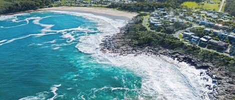 An aerial view of a coastal area with a beach, rocky shoreline, and a residential area with houses.