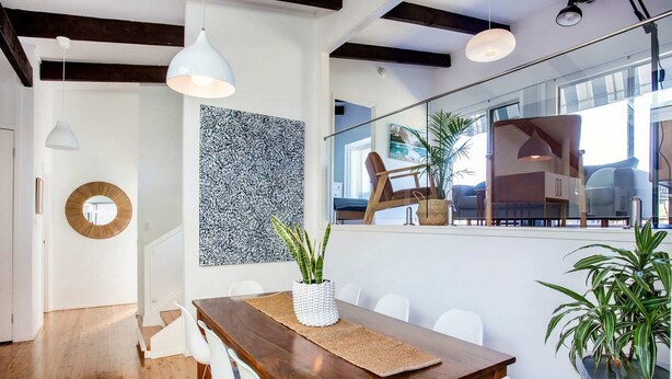Un comedor con mesa de madera, sillas blancas y lámparas colgantes.