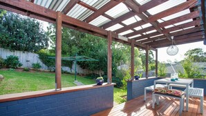 Un patio techado con cubierta de madera, pared de ladrillo azul y una mesa con sillas.