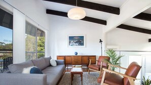 Una sala de estar moderna con un sofá gris, una mesa de centro de madera, un sillón de cuero marrón y un amplio ventanal con vistas a árboles.
