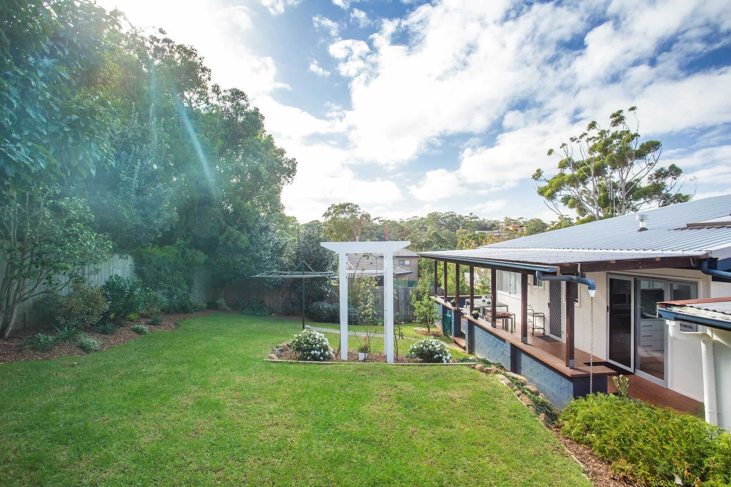 A modern house with a covered patio, a lawn, and surrounding greenery.