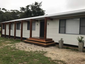 A single-story mobile home with a porch, windows, and a small garden area. - Narrawallee Holiday House (Narrawallee)