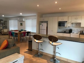 A modern kitchen with white cabinets, a central island, and two bar stools. - Narrawallee Holiday House (Narrawallee)