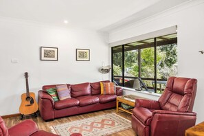 A living room with a red leather sofa, a wooden coffee table, a red leather armchair, a guitar, and two framed pictures on the wall. - Sandy's Beach Shack at Bawley (Bawley Point)