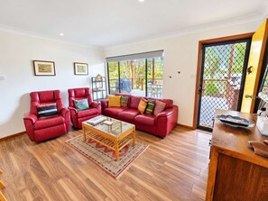 Un salon avec un canapé en cuir rouge, deux fauteuils en cuir rouge, une table basse en verre et une table d’appoint en bois.