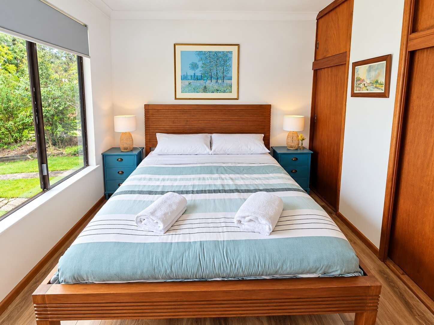 Ein Schlafzimmer mit einem großen Bett, zwei Nachttischen, einem Fenster und einem Gemälde an der Wand.