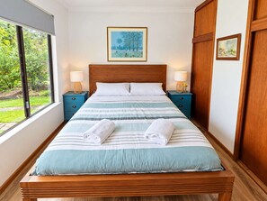 A bedroom with a large bed, two bedside tables, a window, and a painting on the wall.