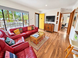A modern living room with a red leather sofa, a glass coffee table, and a television on a wooden cabinet.
