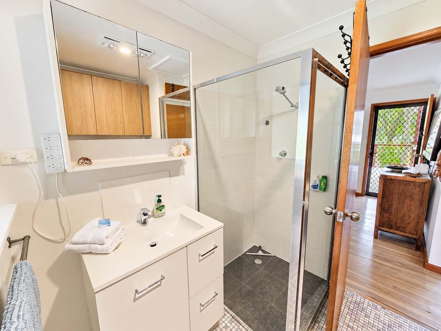 A modern bathroom with a glass shower enclosure, a white vanity with a mirror, and a wooden cabinet.