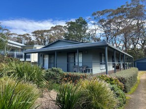 A single-story building with a covered porch, surrounded by native vegetation and trees. - Bawley Beach Bungalow (Bawley Point)