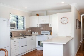 A modern kitchen with white cabinets, a microwave, a stove, and a sink.
