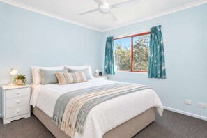 A bedroom with a bed, nightstand, lamp, and window with curtains.