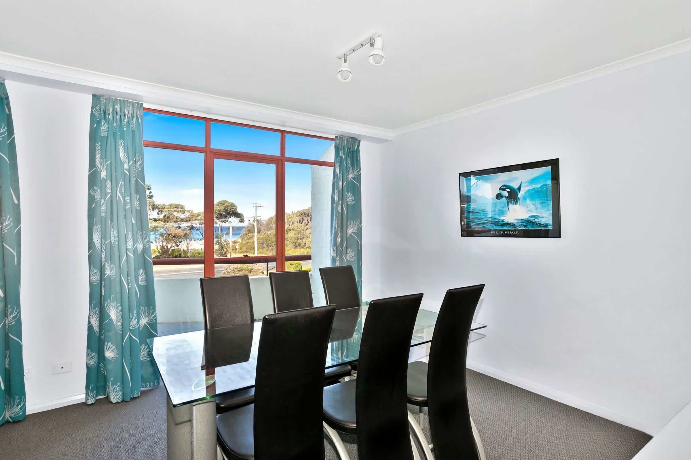 A conference room with a glass table, black chairs, a framed picture of a whale, and a view of the sea through large windows.
