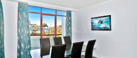 A conference room with a glass table, black chairs, a framed picture of a whale, and a view of the sea through large windows.