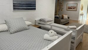 Een moderne slaapkamer met een bed, een witte baksteenmuur, een schilderij van een zeegezicht en een grijze bank op de achtergrond.