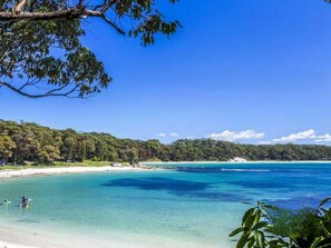 A beach with clear turquoise waters, a sandy shore, and dense green forest in the background. - Neptune's at Manyana (Manyana)