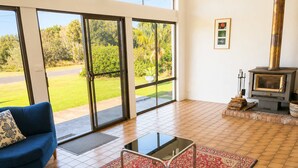 Un salon avec un canapé bleu, une table basse en verre, un tapis rouge à motifs, une cheminée et une vue sur un jardin, visible à travers de grandes portes-fenêtres coulissantes.