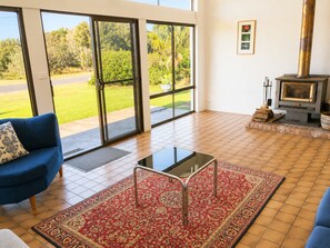 A living room with a blue sofa, a glass coffee table, a red patterned rug, a fireplace, and a view of a garden through large sliding glass doors. - Ocean Front on Malibu (Bawley Point)