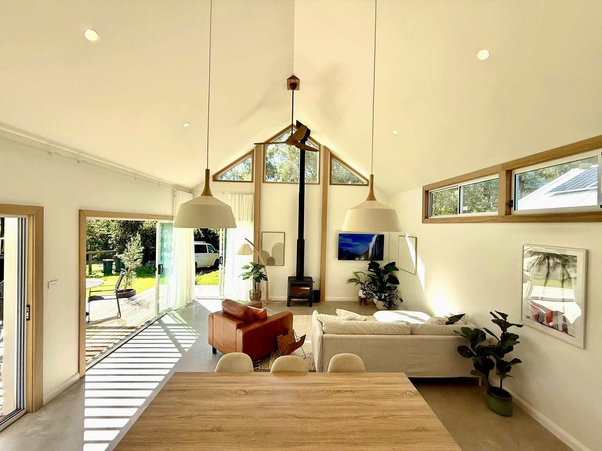 A spacious living area with a large wooden table, two sofas, and a TV. There are large windows and a view of the outdoors.