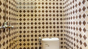 A small bathroom with a toilet, shower, and a tiled wall with a diamond pattern. - Life Lavenia Kost 2 (Dumai)