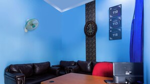 A room with a wooden desk, black leather sofa, a red chair, a clock, and a wall with emergency contact numbers. - Life Lavenia Kost 2 (Dumai)