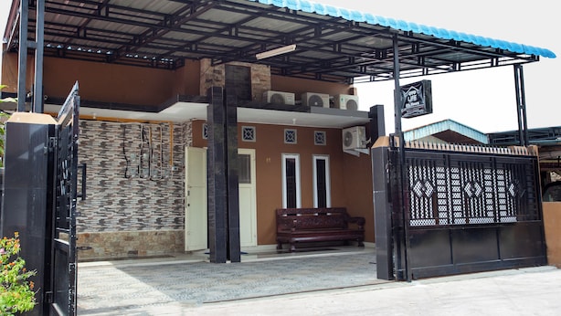 A building with a covered entrance, a stone wall, and a gate. - Life Lavenia Kost 2 (Dumai)