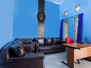 Ein Zimmer mit blauer Wand, einem braunen Ledersofa, einem Holztisch und einem roten Sessel.