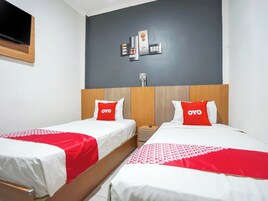 Habitación de hotel con dos camas, cada una con una colcha roja y blanca, y una pared gris con una obra de arte encima.