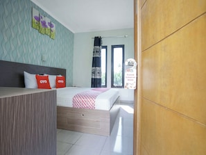 Quarto de hotel com cama, secretária, parede com pintura floral e janela com cortinas.