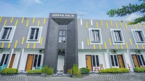 Un edificio con el letrero 'GREEN PALM' en la parte superior, que presenta un diseño arquitectónico moderno con una entrada central y múltiples ventanas en cada planta.