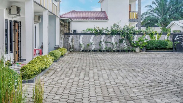 Un patio con suelo empedrado, un edificio blanco con tejado rojo y una pared de piedra con vegetación.