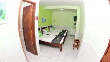 Een kamer met een houten deur, een bed met groene beddengoed, een klein krukje en een lijst met een afbeelding aan de muur.