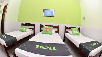A hotel room with three single beds, each with a green and white bedspread and a pillow with a letter.
