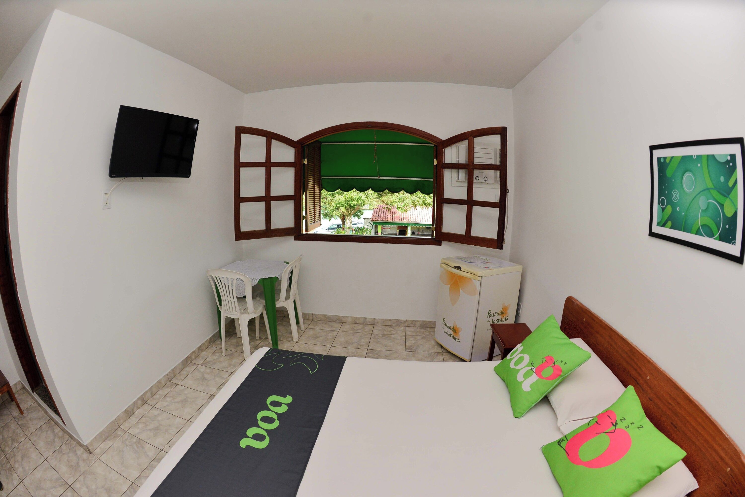 Una habitación pequeña con cama, escritorio, silla, televisor y ventana con persiana abierta.