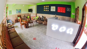Una habitación con recepción, un sofá, una mesa de comedor con sillas y un televisor en la pared.