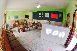 Una habitación con recepción, un sofá, una mesa de comedor con sillas y un televisor en la pared.