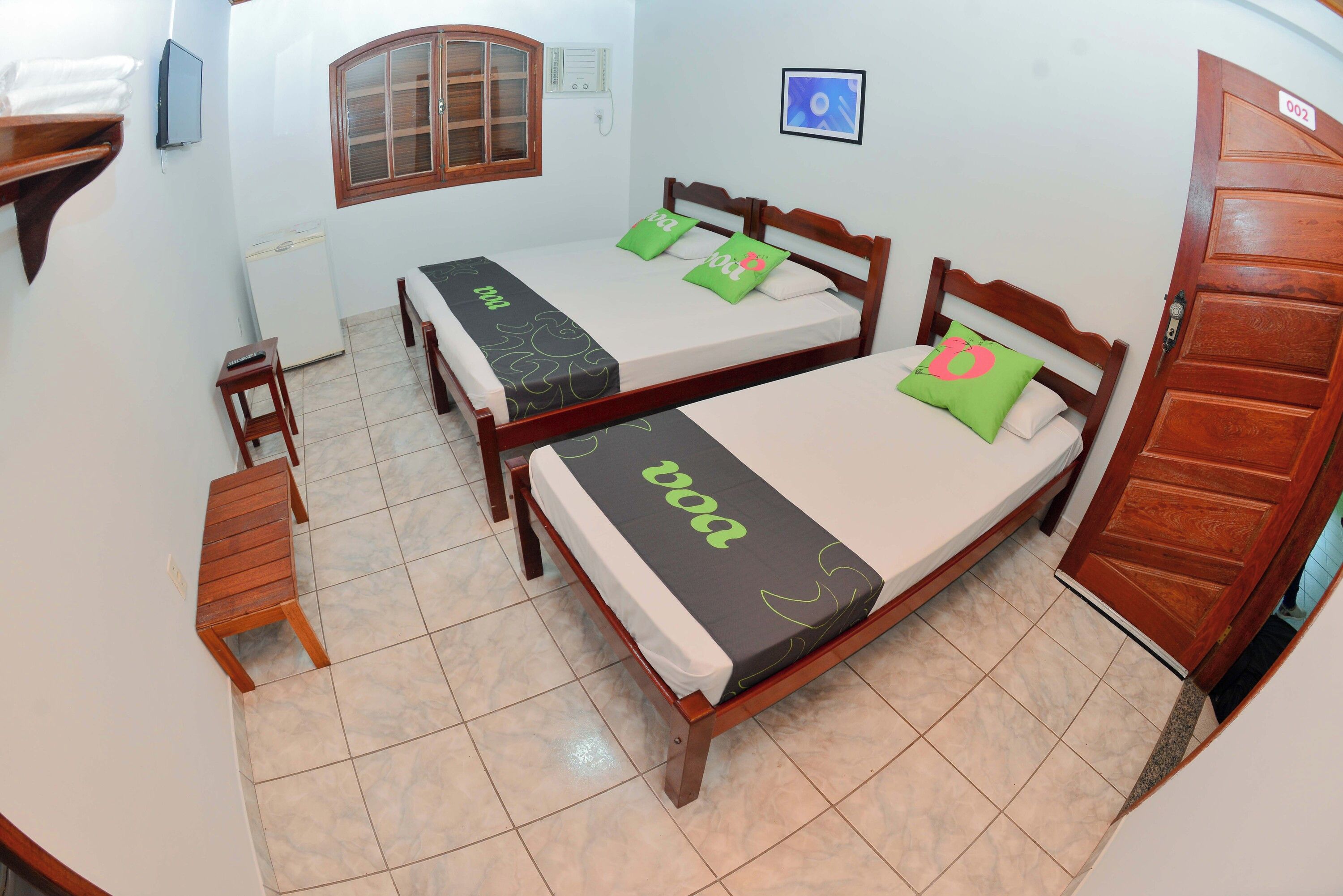 A room with two wooden beds, a small table, a wall-mounted TV, and a door with a number.