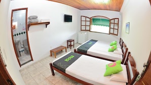 Una habitación con dos camas, una mesita, un espejo y una ventana con una persiana abierta.