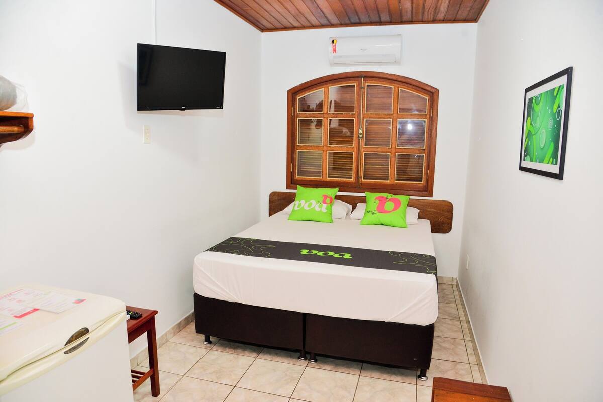 Un dormitorio con cama, televisor, ventana y aire acondicionado instalado en la pared.