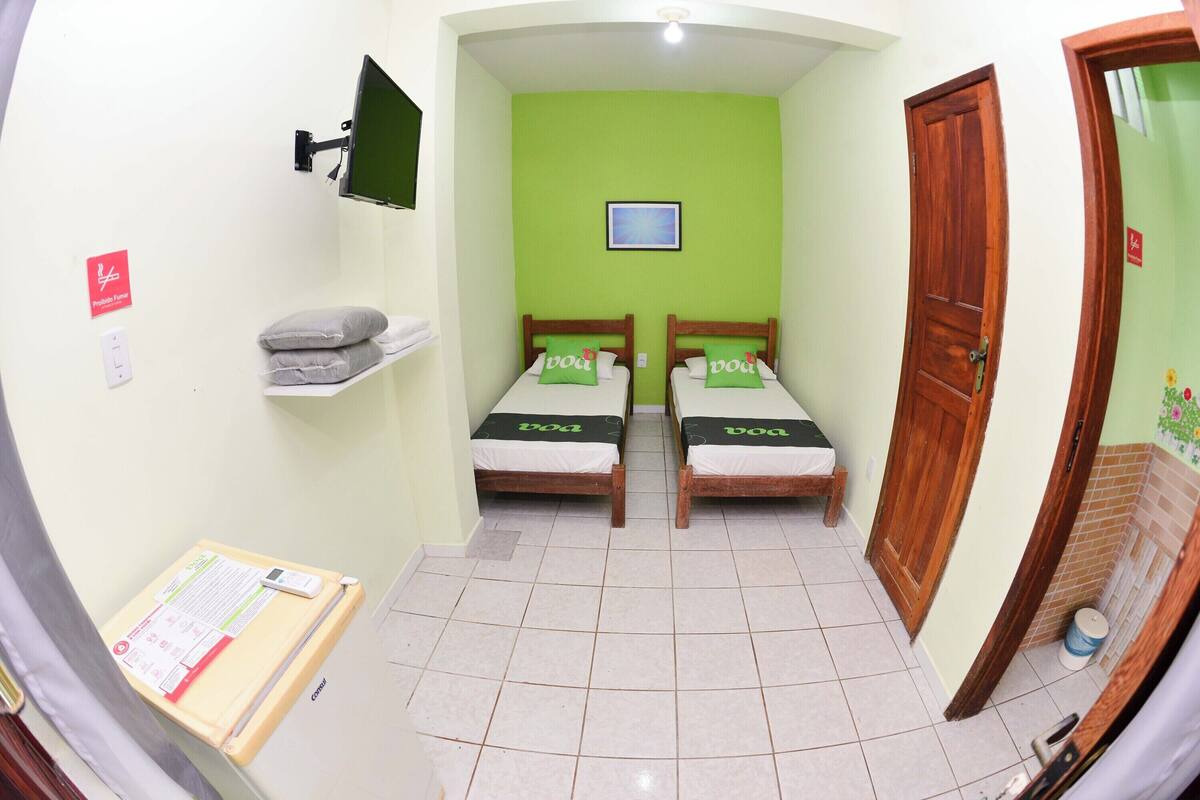 Una habitación pequeña y estrecha con dos camas, un televisor montado en la pared y una puerta que da a otra habitación.