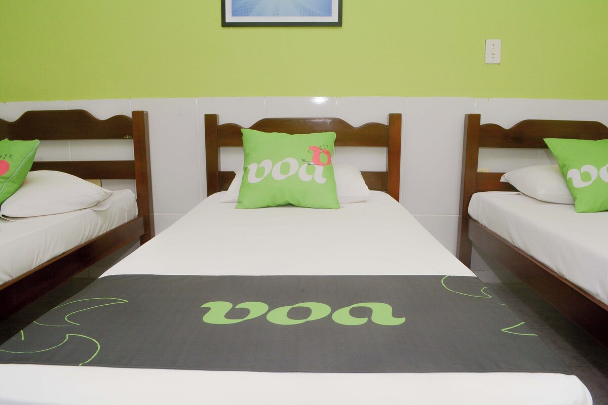 A hotel room with two beds, each with a wooden headboard, a green pillow, and a bedspread with the word 'voa' printed on it.
